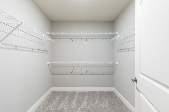 a spacious walk in closet with white wire shelving and a carpeted floor