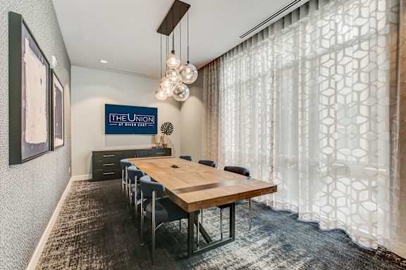 A conference room with a long table and chairs, a carpeted floor, and a large window with patterned curtains.