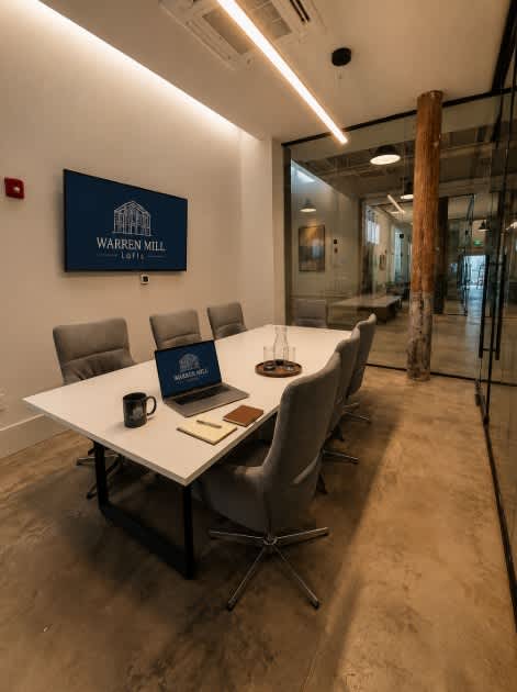 A conference room with a laptop on the table and a sign that says Warren Mill.