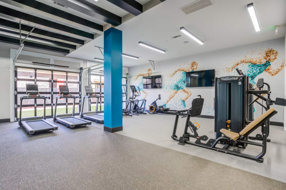 a gym with cardio equipment and a wall with a mural