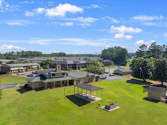 A large building with a covered patio is surrounded by a grassy area and other buildings.