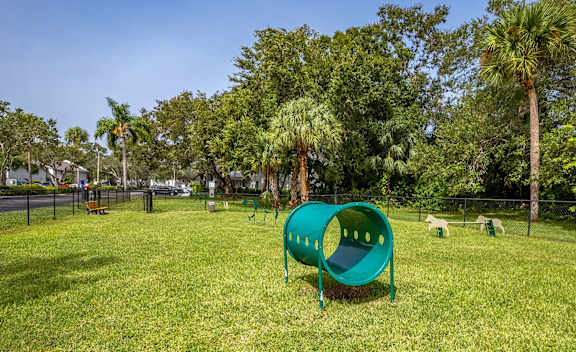 A playground with a green tunnel-like structure in the middle of a grassy area.