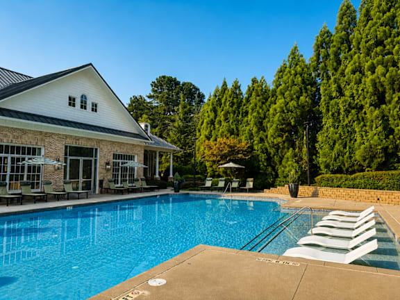 A swimming pool with lounge chairs and a house in the background.