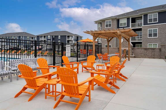 A patio with orange chairs and a wooden pergola.
