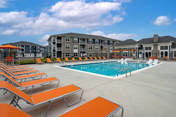 A swimming pool surrounded by orange sun loungers and a building in the background.
