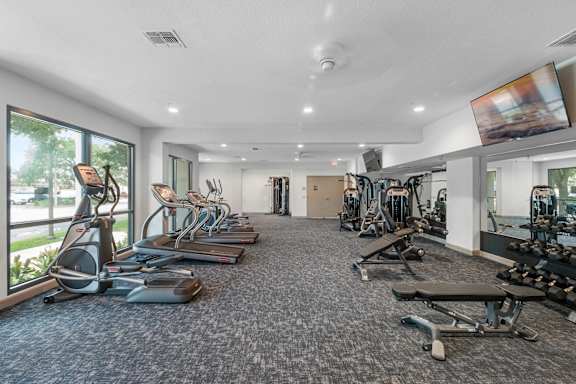 A spacious gym with a variety of exercise equipment and a flat screen TV mounted on the wall.