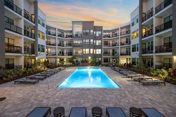 A large swimming pool surrounded by lounge chairs and balconies of apartment buildings.