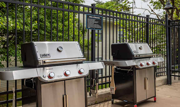 Two grills are placed next to a fence.