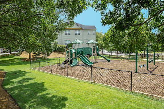 A playground with a green slide and a fence.