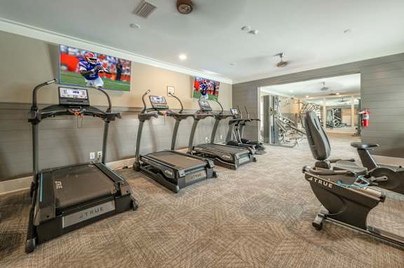 A gym with treadmills and a television showing a football game.