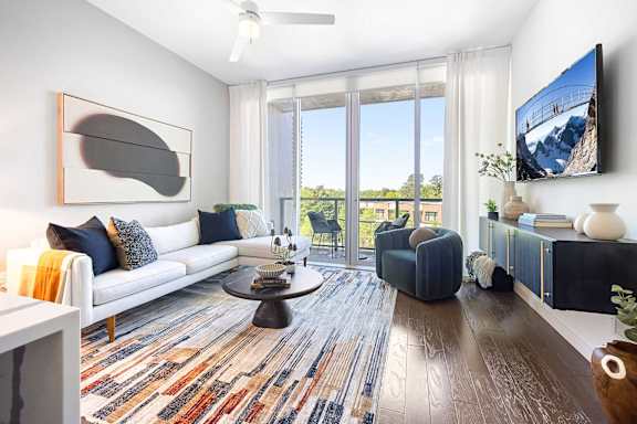 A living room with a white couch, a coffee table, and a flat screen TV mounted on the wall.