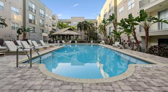 A swimming pool surrounded by lounge chairs and palm trees.