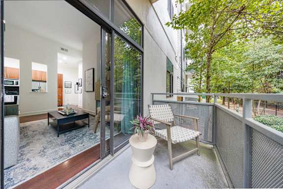 A balcony with a chair and table overlooking a tree.