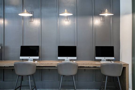 Three computers are on a table with chairs.