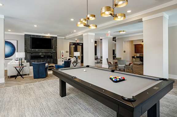 A pool table with a set of balls on it in a room with a television and a trash can.