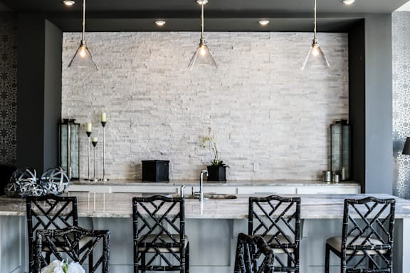 A kitchen with a white brick wall and black chairs.
