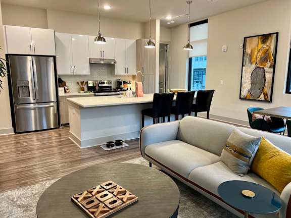 A modern kitchen with a white fridge and a grey couch with a yellow pillow.