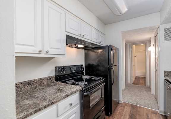 A black fridge and stove in a kitchen with white cabinets.