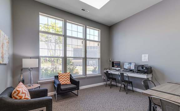 A room with a desk, chairs, and a couch with a window in the background.