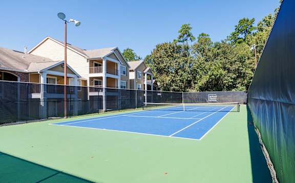 A tennis court is surrounded by apartment buildings.