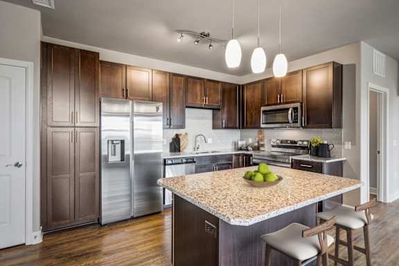 A kitchen with a granite countertop and a bowl of green apples on it.