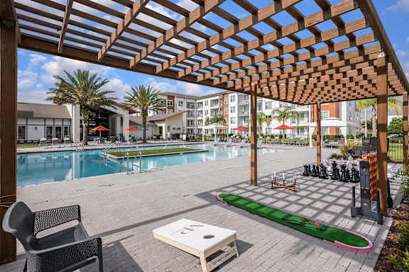 A wooden pergola over a poolside area with a lounge chair and a table.