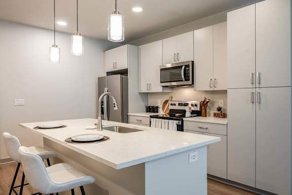 A kitchen with a white countertop and white chairs.