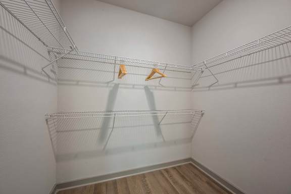 A white closet with two hangers and a wooden floor.
