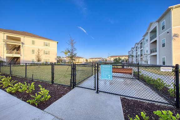 A fenced area with a sign and a bench in front of apartment buildings.