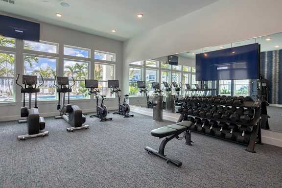 A gym with a row of treadmills, elliptical machines, and a bench press.