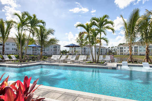 A pool surrounded by palm trees and lounge chairs.