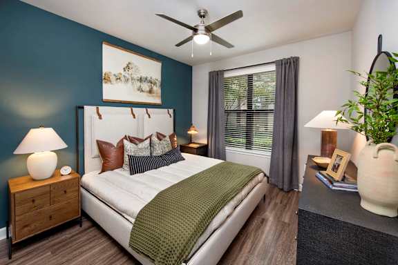 A bedroom with a bed, nightstand, and a plant.