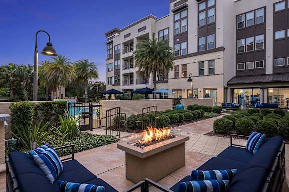 A fire pit sits in the middle of a patio surrounded by blue cushioned seating.