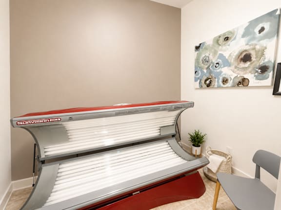 A tanning bed with a red and white cover is in a room with a painting on the wall.
