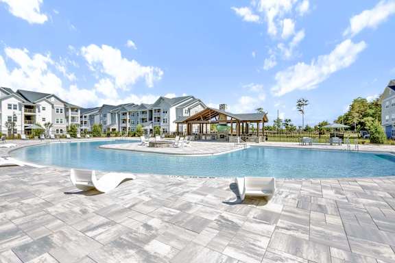A large swimming pool surrounded by a stone patio and lounge chairs.