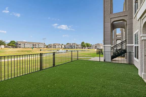 A black fence surrounds a green lawn in front of a building.