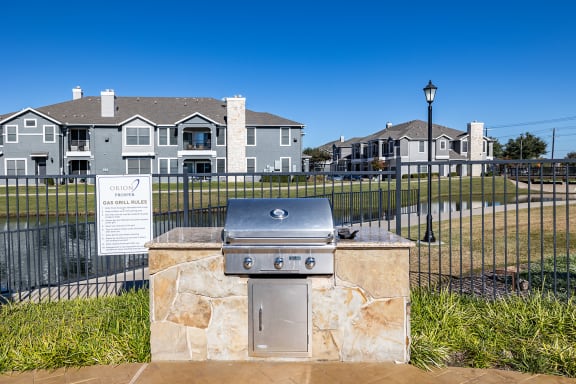 a gas grill in front of a fence with apartments in the background  at Orion Prosper, Prosper, Texas