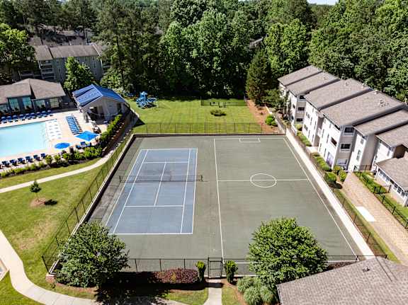 A tennis court is surrounded by trees and apartment buildings.