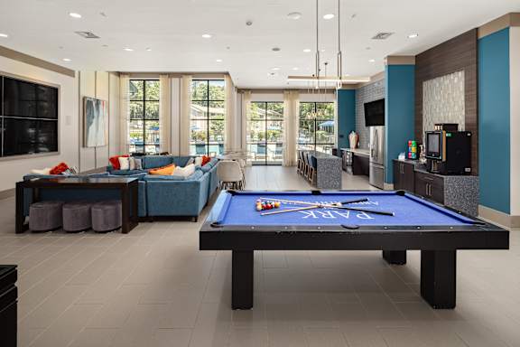 A pool table is in the middle of a room with a bar and a couch.