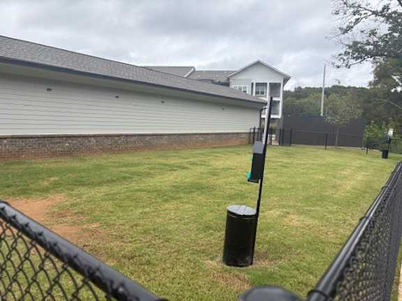 A black fence surrounds a grassy area with a building in the background.