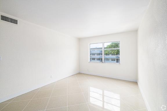 A large empty room with a window and a tiled floor.