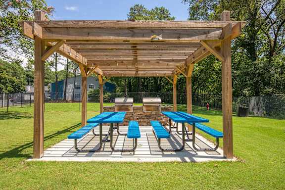 A wooden pavilion with blue benches is set up in a grassy area.