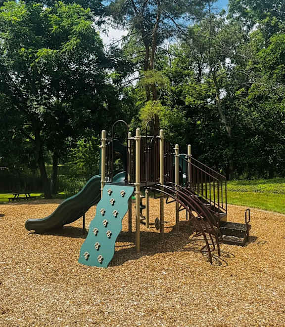 A playground with a green slide and a brown structure.