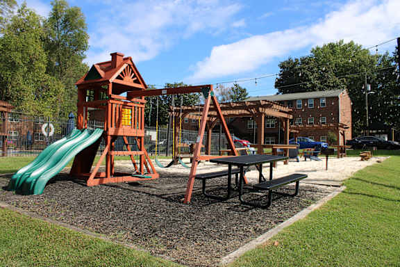 A playground with a green slide and a red wooden playhouse.