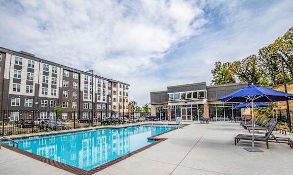 A swimming pool in front of a building with a blue umbrella.