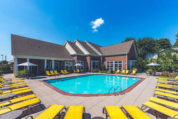 A pool surrounded by yellow sun loungers and a building in the background.