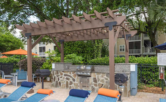 A patio with a grill and chairs under a pergola.