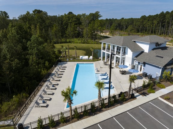 a large swimming pool in front of a house and a building with chairs and trees