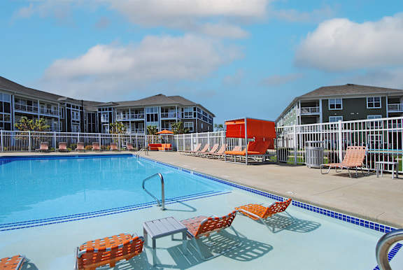 A swimming pool with orange chairs and a red object in the background.
