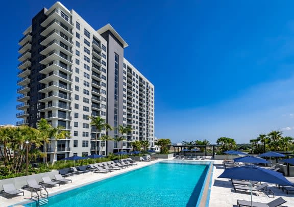 a swimming pool with chaise lounge chairs and umbrellas in front of a tall building at Regatta at New River, Florida, 33301